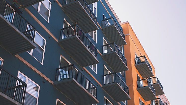 A low-angle view of modern apartments with balconies featuring dark blue and orange facades against a clear sky.