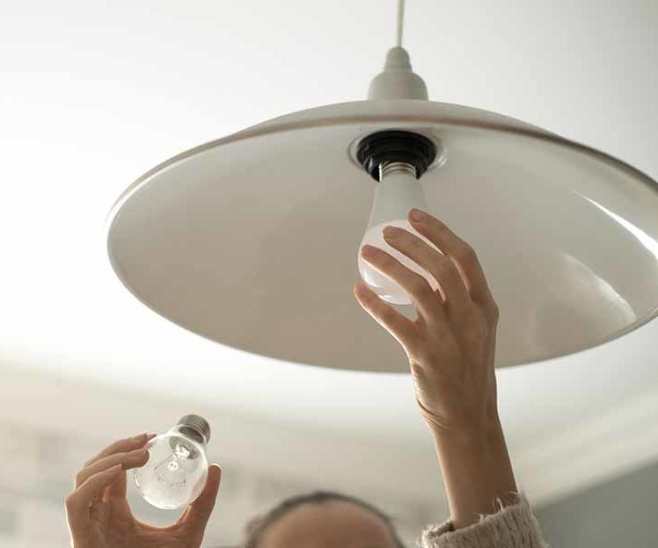 Person changing a light bulb in a ceiling lamp, holding a new bulb and removing the old one.