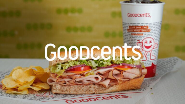 A sub sandwich with chips on the side next to a drink cup with an overlay of the Goodcents logo.