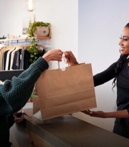 A person handing a shopping bag to a customer over a store counter.