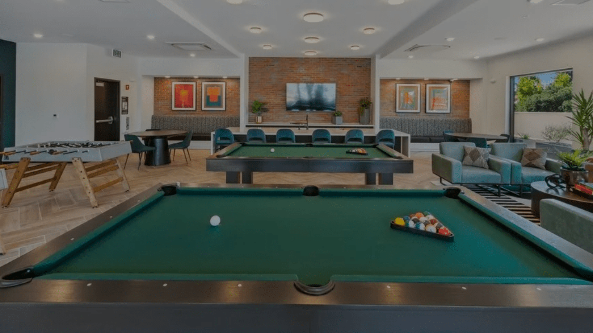 A modern game room with two pool tables, a foosball table, sofas, and artwork on the walls.