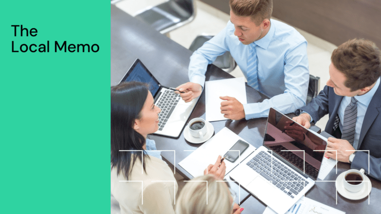 Four people in business attire have a meeting with laptops, coffee, and notepads around a table.