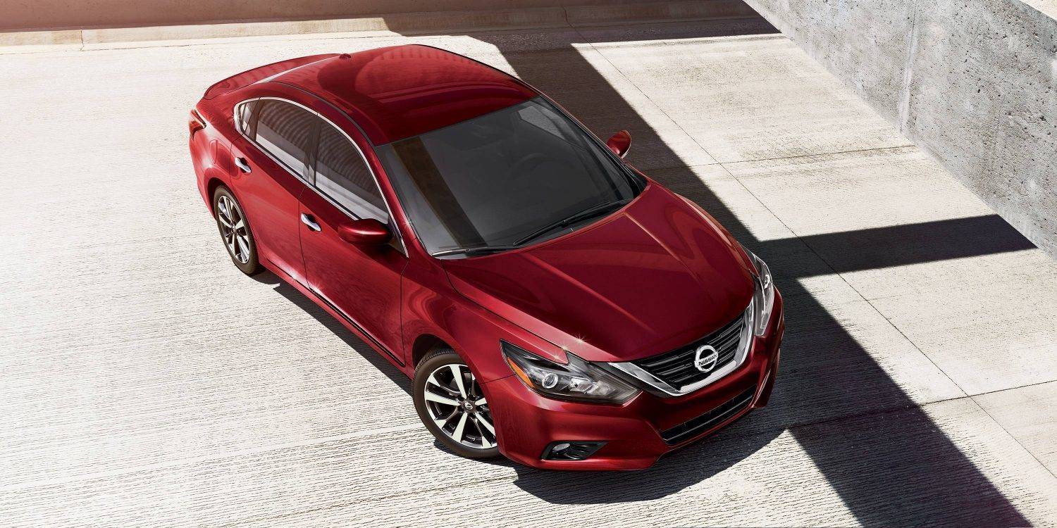 A red sedan parked on a sunlit concrete surface near a gray wall, viewed from above.