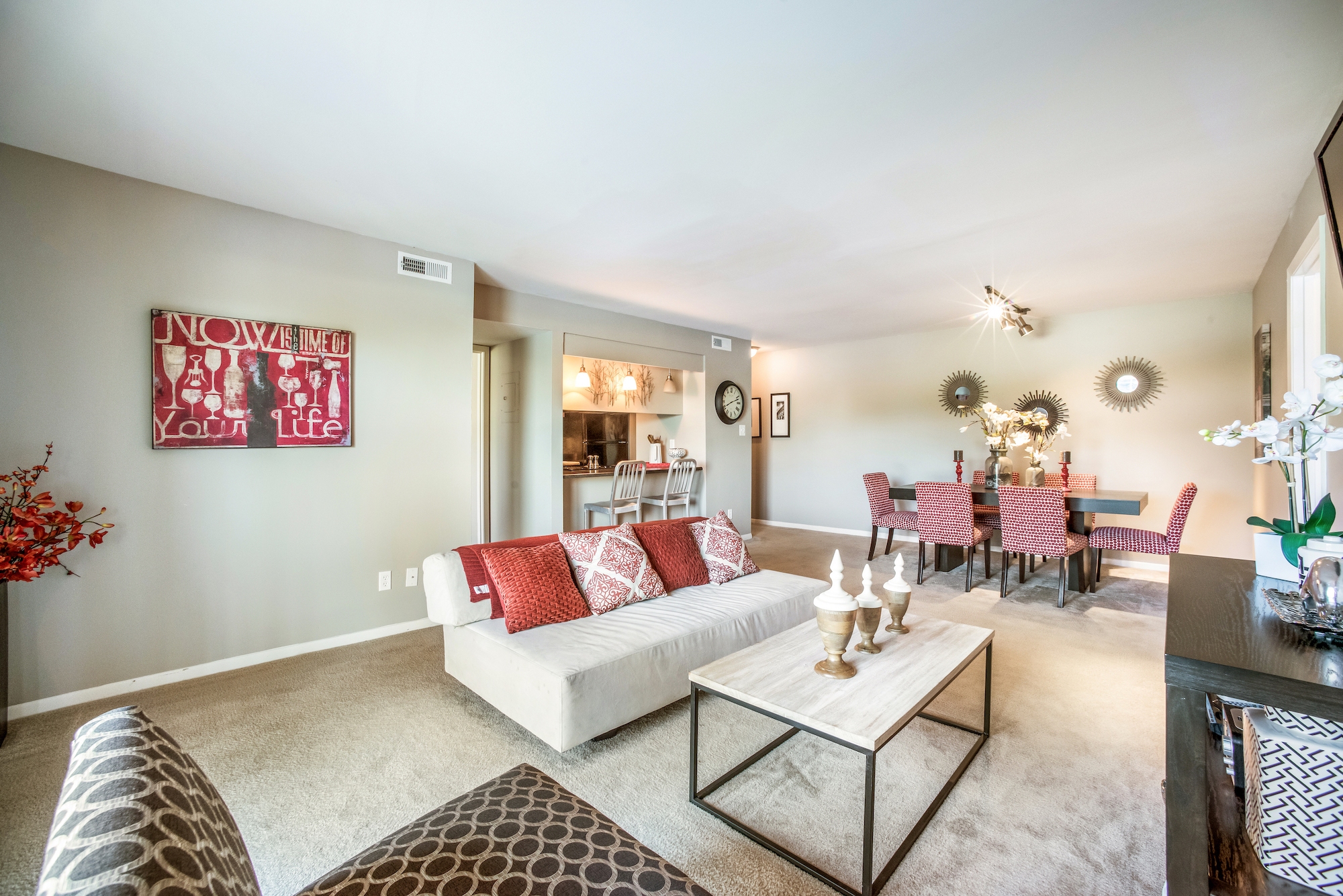 Spacious living and dining area with modern decor, red accents, and neutral-colored furniture.