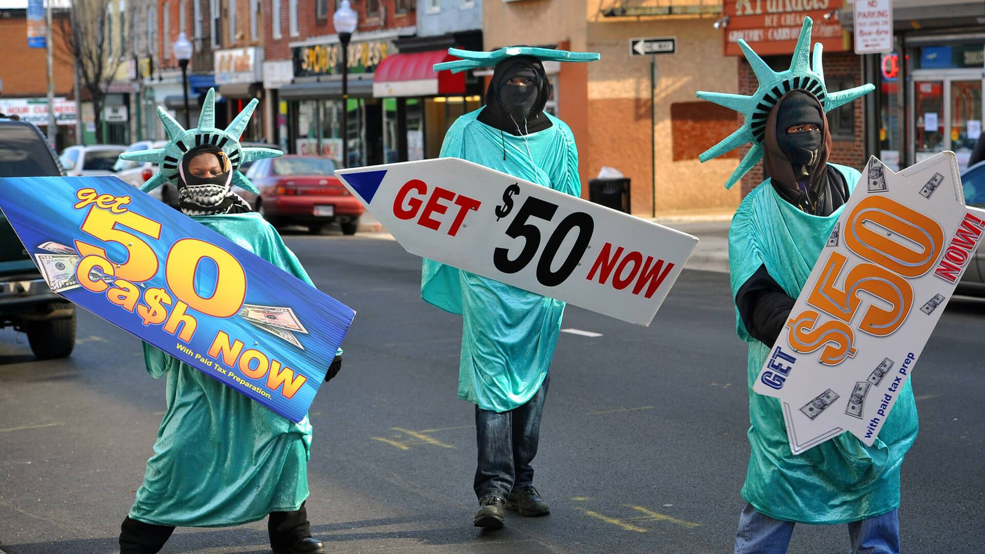 Three people in Statue of Liberty costumes hold signs advertising cash loans on a city street.