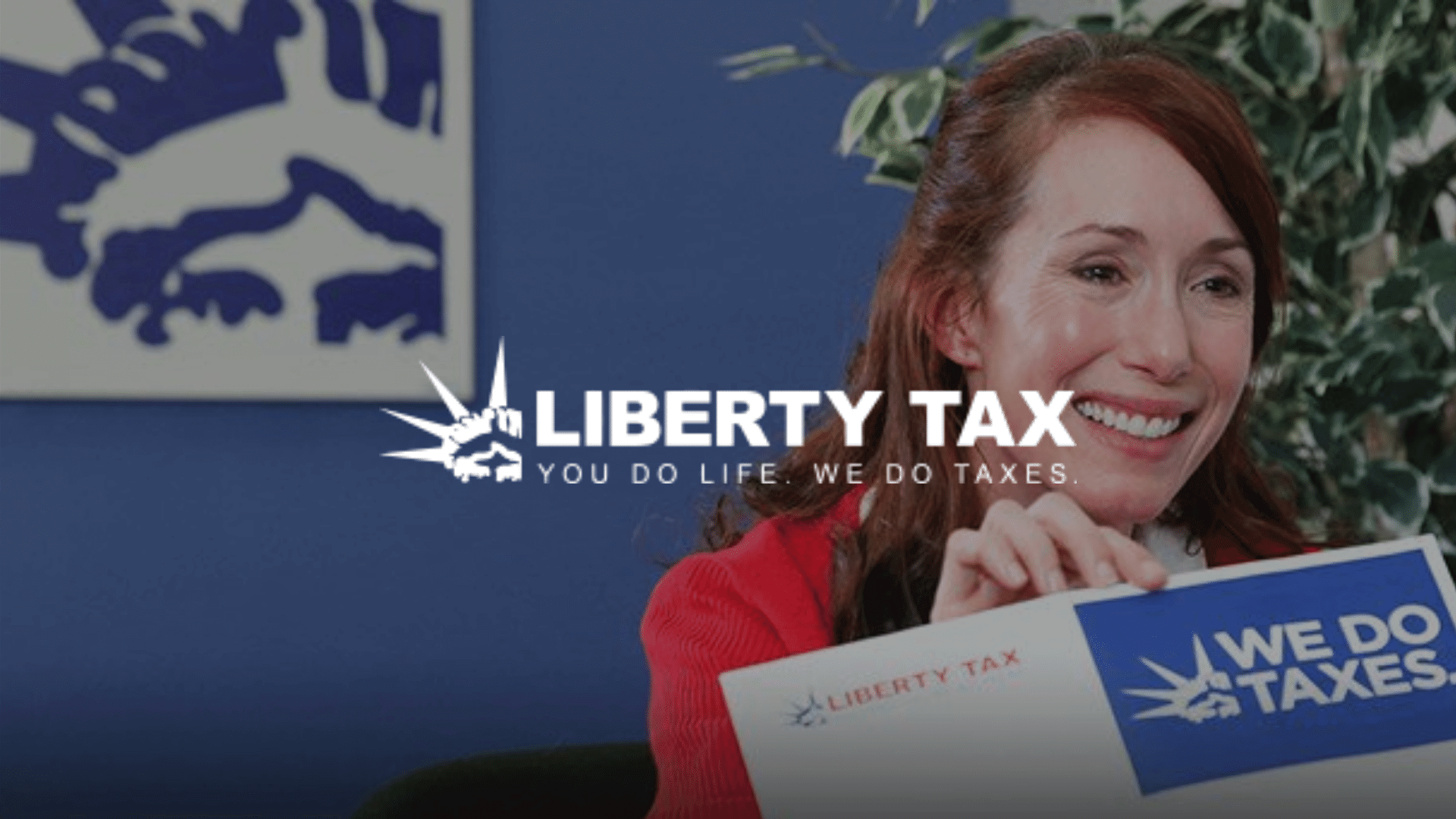 Smiling woman holding a WE DO TAXES sign with Liberty Tax logo and slogan overlayed on the image.