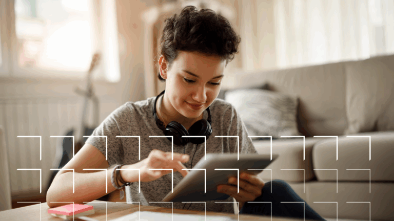 Young person using a tablet at a table with headphones around their neck in a cozy living room.