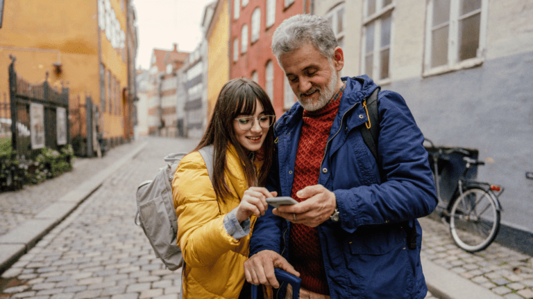 Millennial girl discovering city with her father as both wear coats and backpacks and are looking at phone
